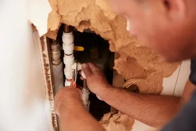 Licensed plumber repairing a concealed burst water pipe inside a residential wall in Emerald, Queensland.