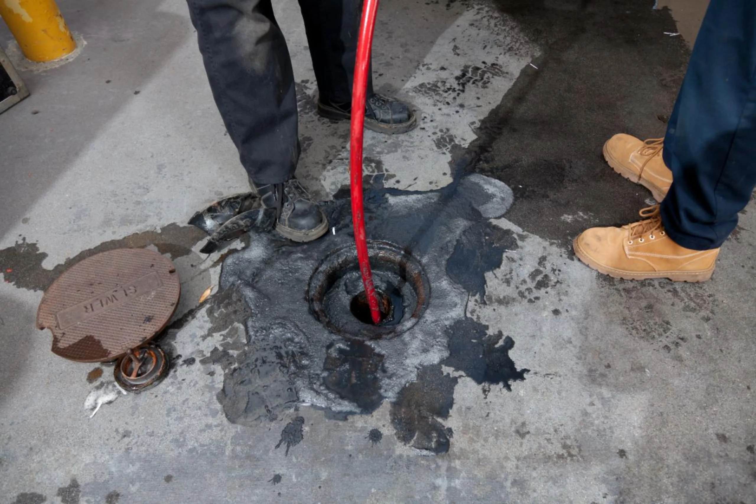 High-pressure water jetting hose clearing a clogged sewer drainage pit and ground overflow.